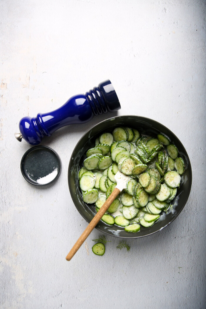 cucumber dill salad in a bowl with salt dish and pepper on the side.