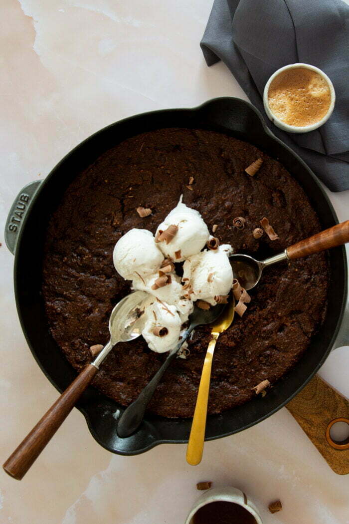 Mocha brownies veganos hechos en un sarten con bolas de nieve y cucharas alrededor.