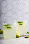 Two glasses of lime mezcal margarita on a marble table.