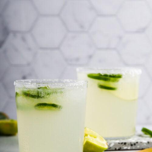 Two glasses of lime mezcal margarita on a marble table.