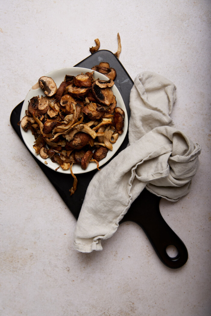 Champiñones fritos en freidora de aire en un plato blanco sobre una tabla de madera.