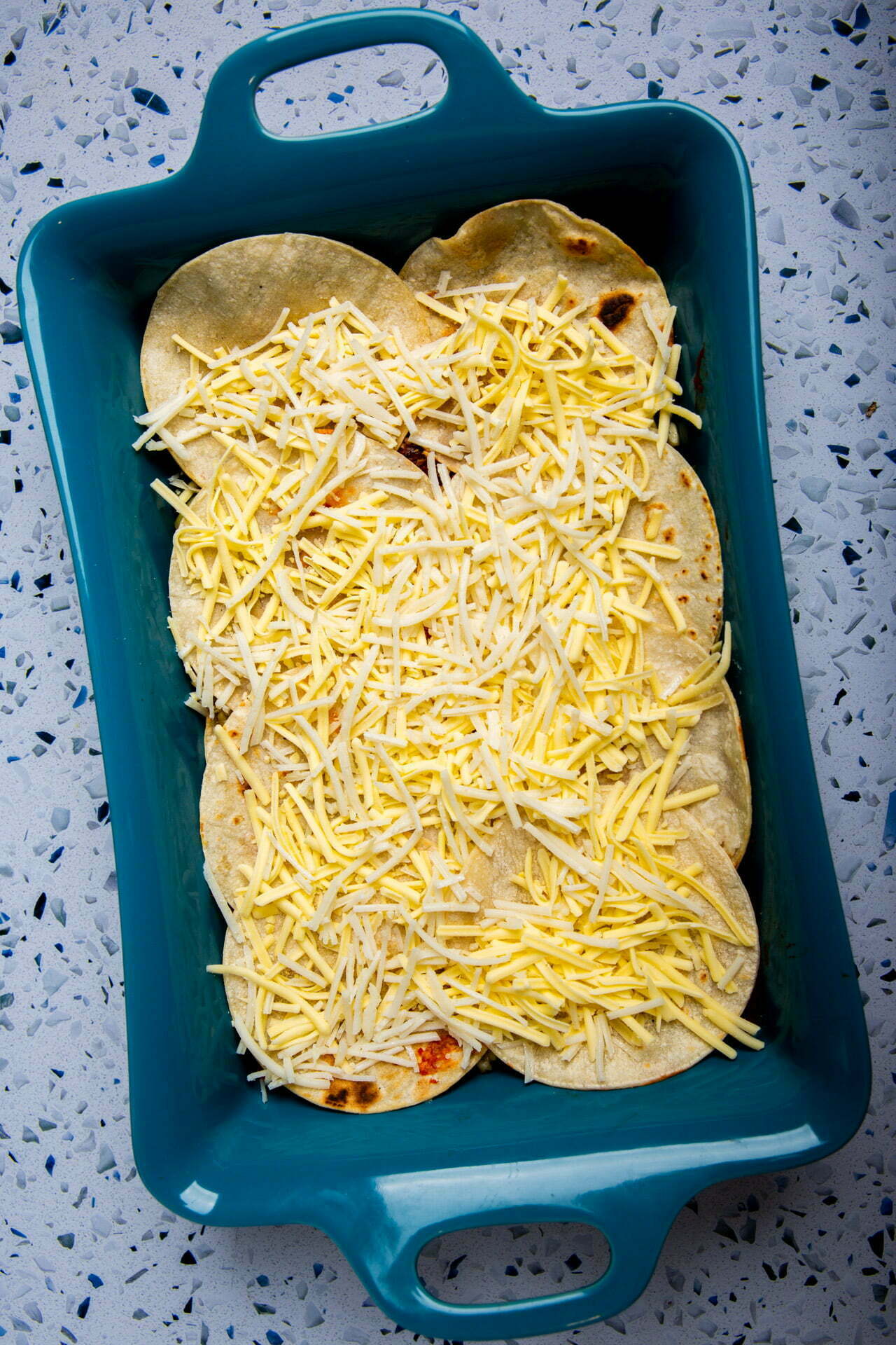 Baked vegan enchilada casserole with bubbly melted cheese and red guajillo sauce in a ceramic dish