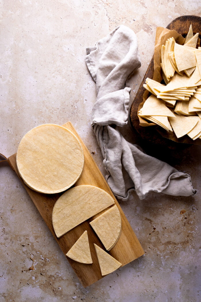 tortillas de maíz sobre tabla de madera cortadas y una batea de madera con pedazos de tortillas de maiz.