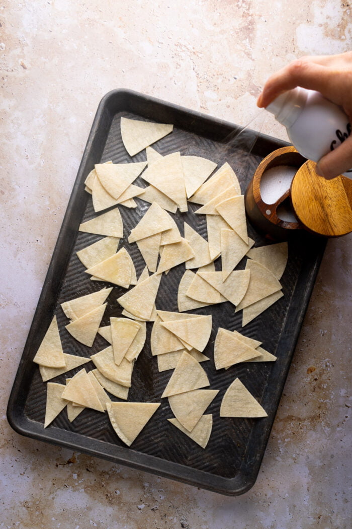 tortilla cortada en triangulos esta siendo rociada con aceite en spray y sal.