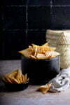 A bowl and a small dish filled with crispy Air Fryer tortilla chips on a dark backdrop.