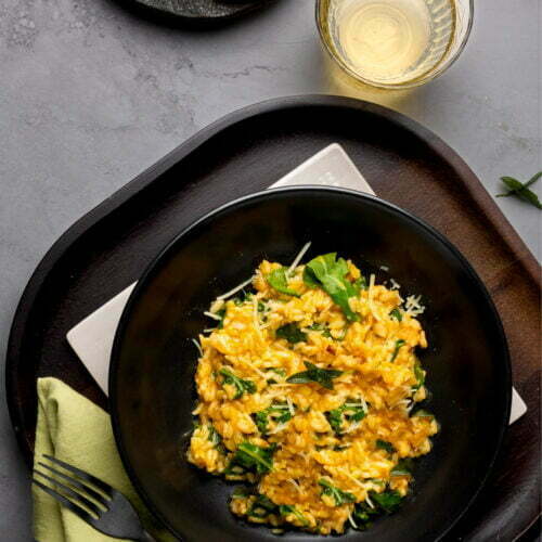 A black bowl with oven-baked risotto and bread on a table.