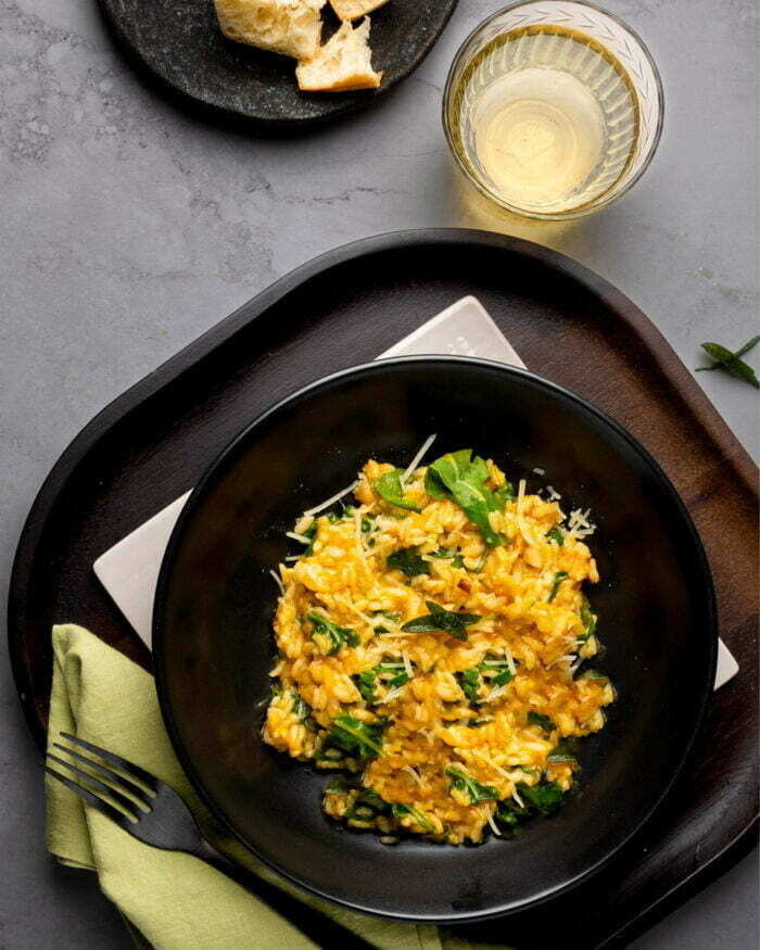 Risotto de calabaza al horno con hojas de salvia fritas sobre un bowl de ceramica negra.