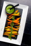 A plate of roasted carrots with a green sauce on it.