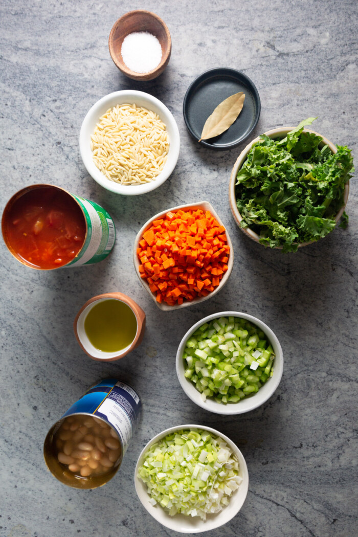 dry pasta, kale, salt, onion, canned tomato, olive oil, celery and beans measured and in small plates.
