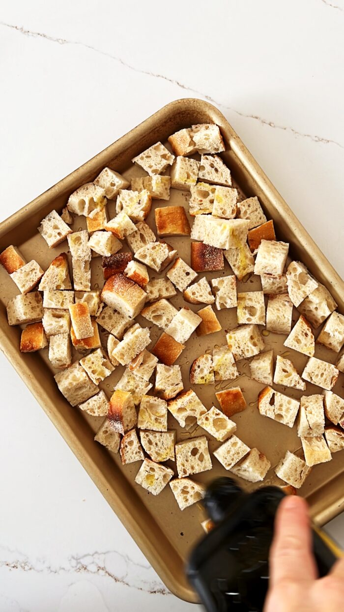 Baking sheet with cubed bread being drizzled with olive oil