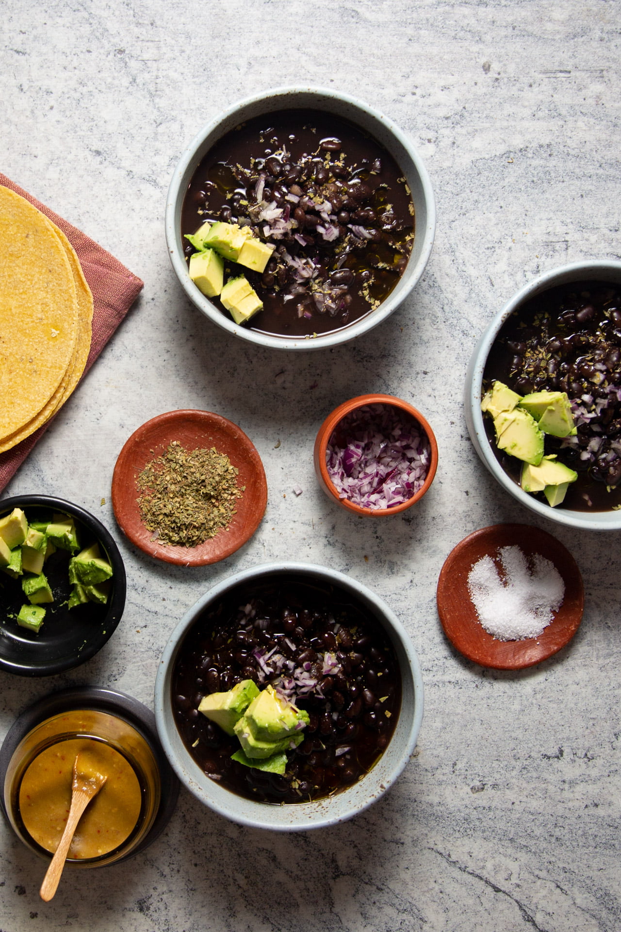 frijoles de olla, 3 bowls with cooked black beans and little dishes with onions, oregano and salt.