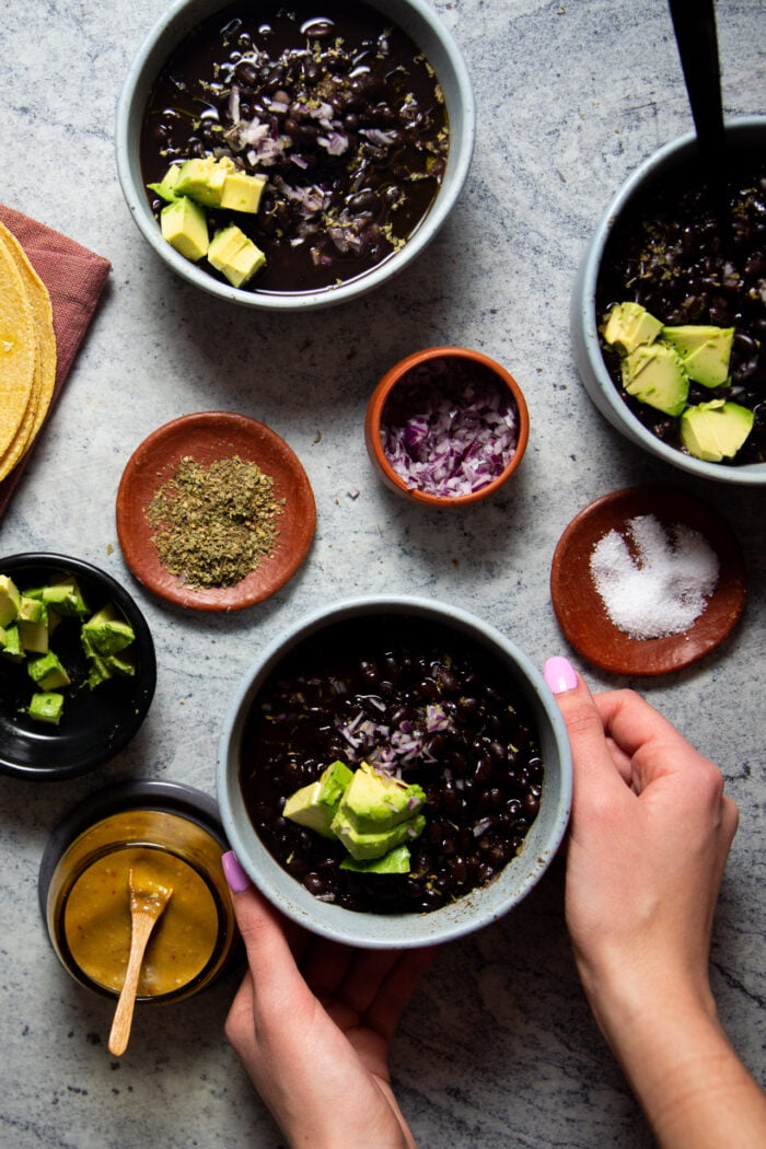 frijoles de olla in a bowl topped with avocado slices, and red onion