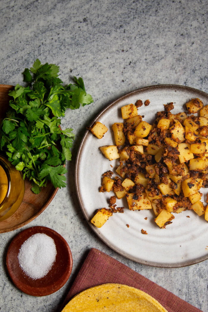 papas con chorizo on a plate next to fresh cilantro and a bowl of salsa
