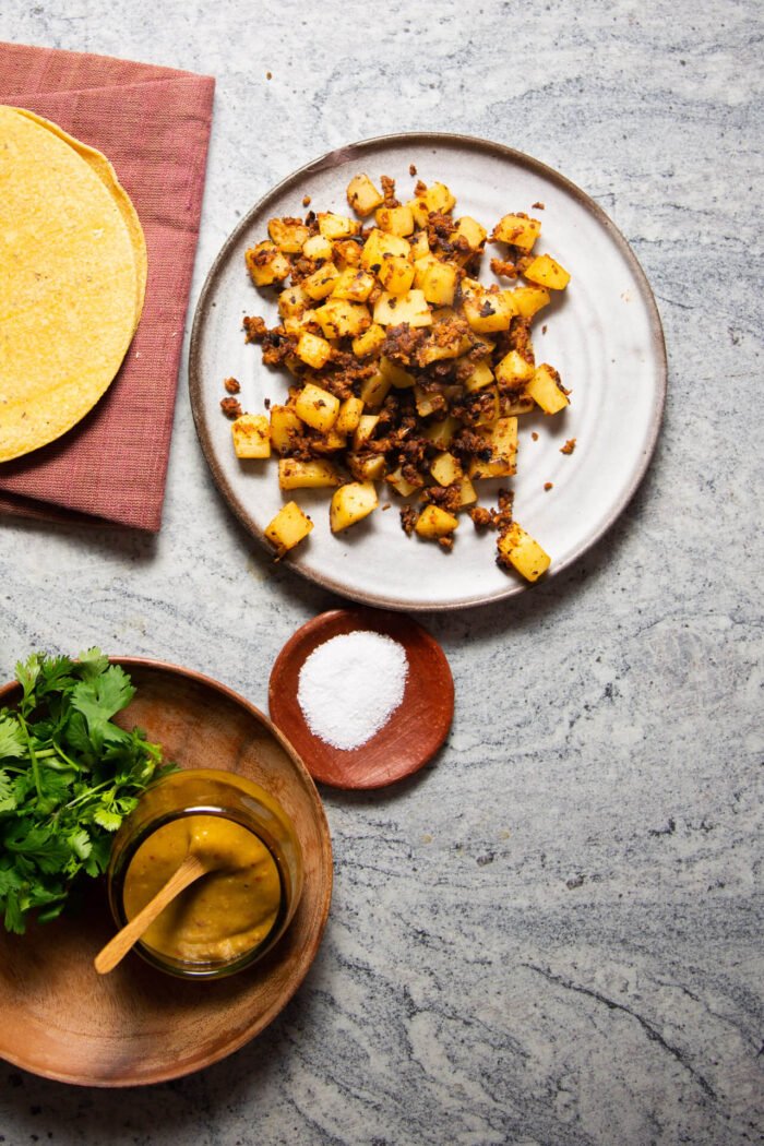 papas con chorizo on a plate nest to corn tortillas, fresh cilantro and a mini bowl of salsa