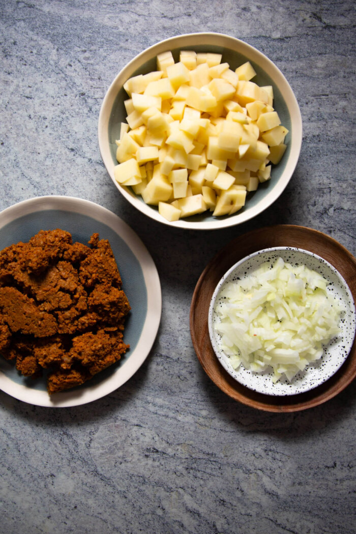 a bowl with diced potatoes, a plate with chorizo and a small plate with diced onions