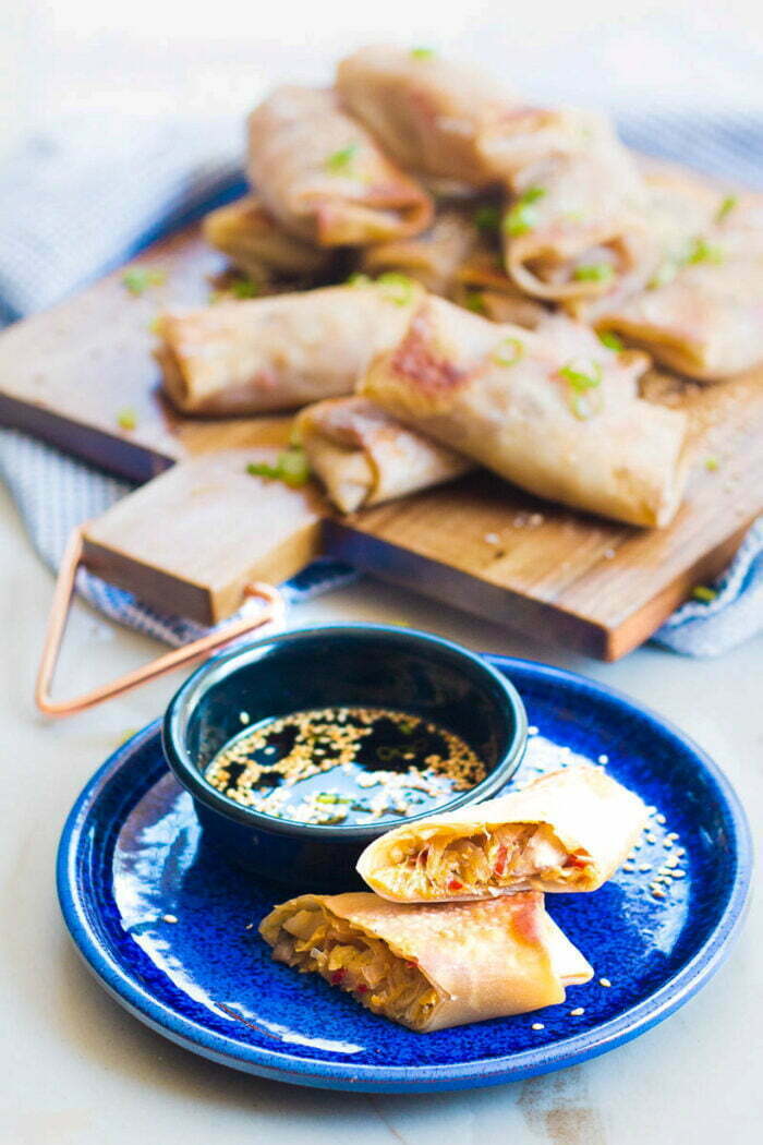 Egg roll halved on a blue plate and dipping sauce.