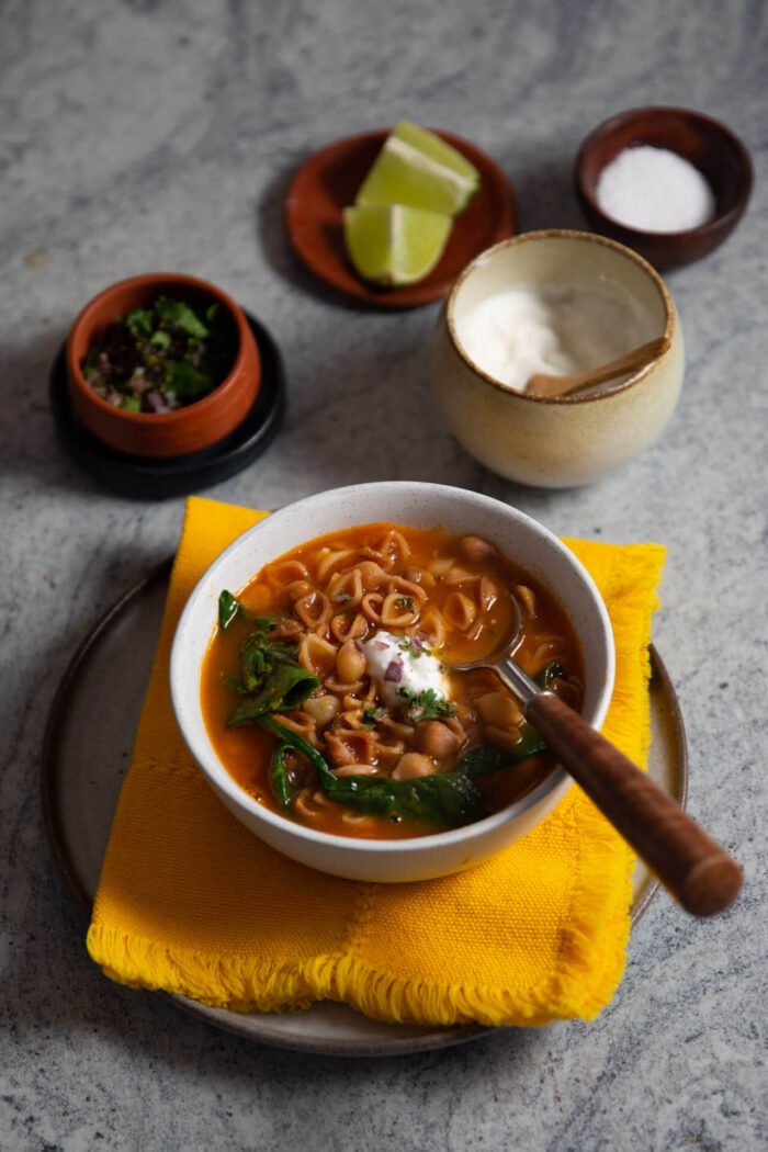 mexican vegan sopa de conchas in a bowl over a yellow napkin with a dollop of vegan sour cream and wilted spinach.