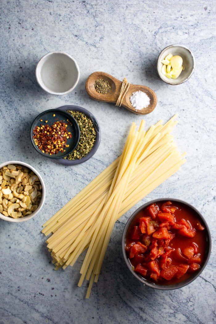 Chopped canned tomatoes, raw cashews, oregano and garlic in bowls for vodka pasta sauce.