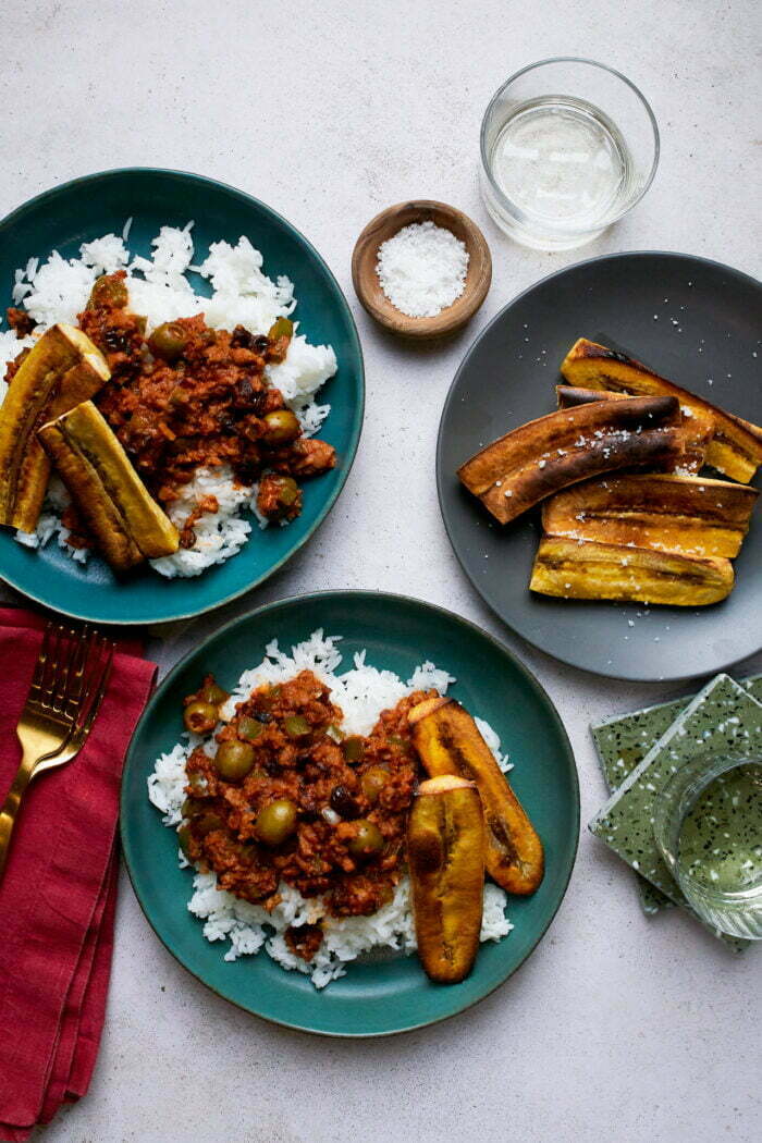 Two plates with white rice topped with cuban picadillo and plantains.