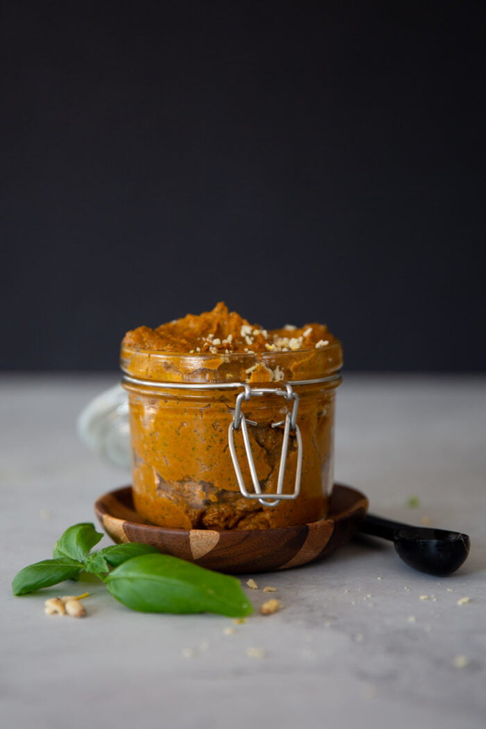 sun dried tomato pesto  oin a small jar over a small wood plate and a leave of basil.