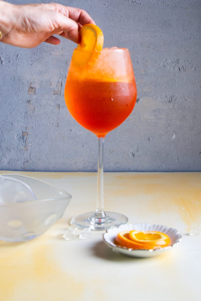 Adding a slice of orange to a glass with aperol spritz