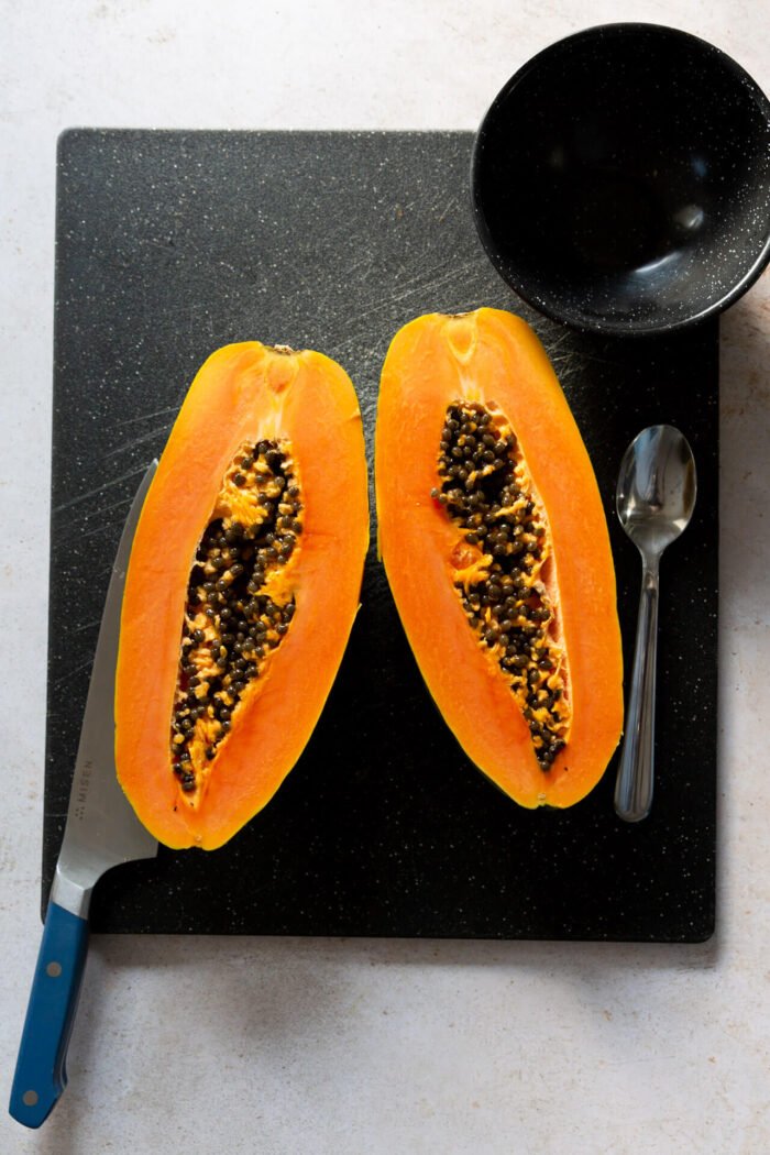 papaya cut in half over a black cutting board