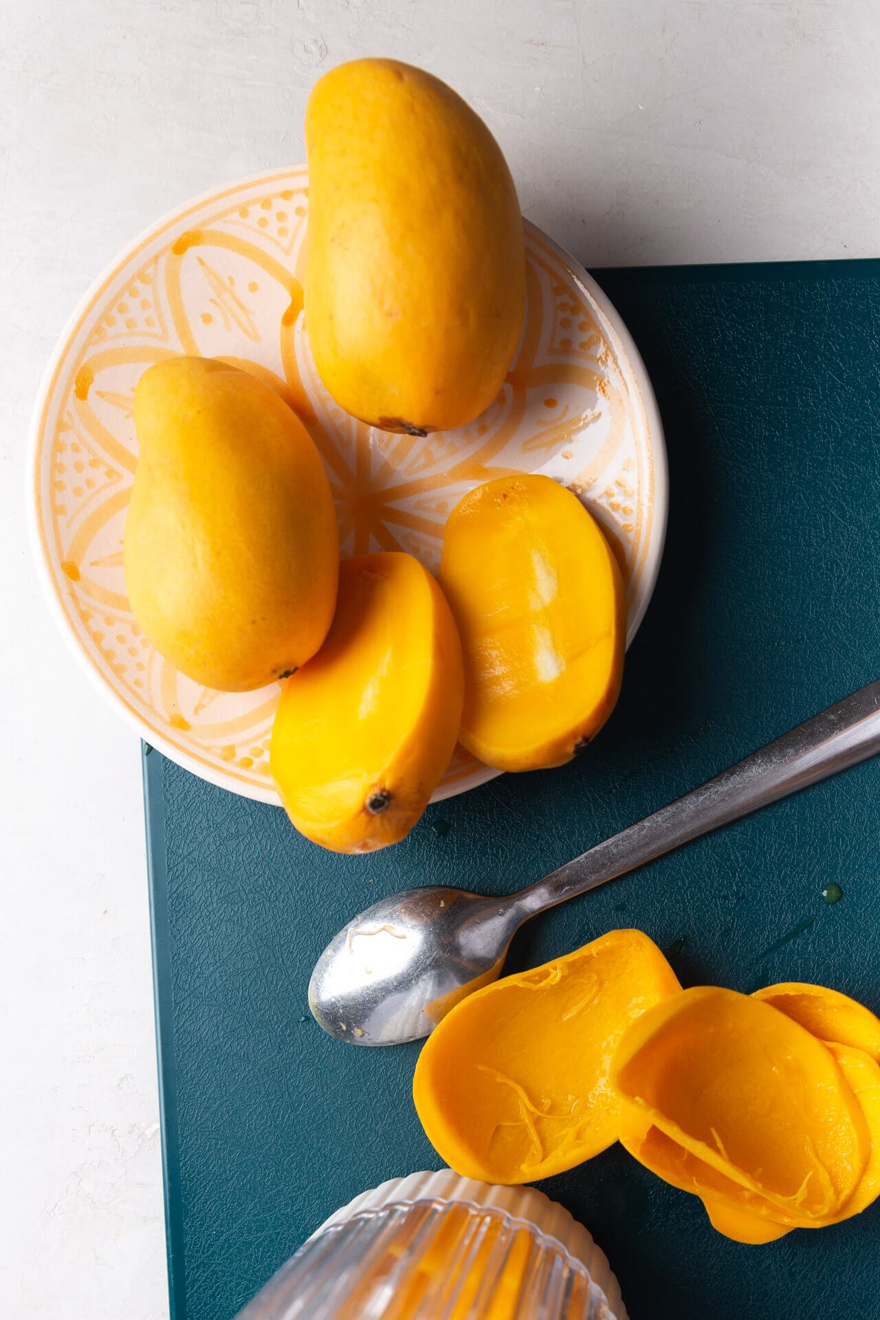 mangoes and halved mangoes over a green cutting board