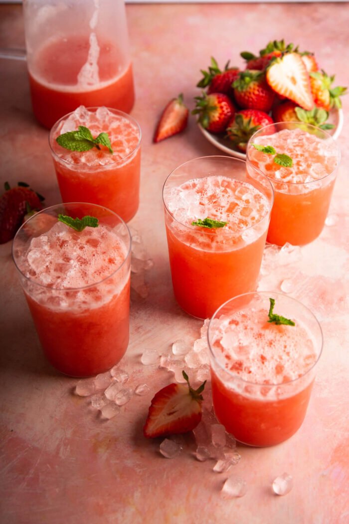 Several cups with agua de fresa (straberry agua fresca) with ice and topped with fresh mint leaves