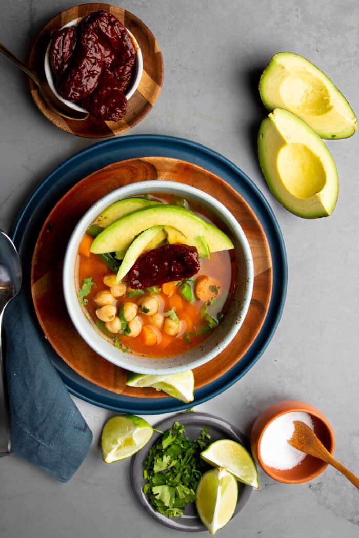 vegan tlalpeno broth on a plate with cilantro and lemons on the side