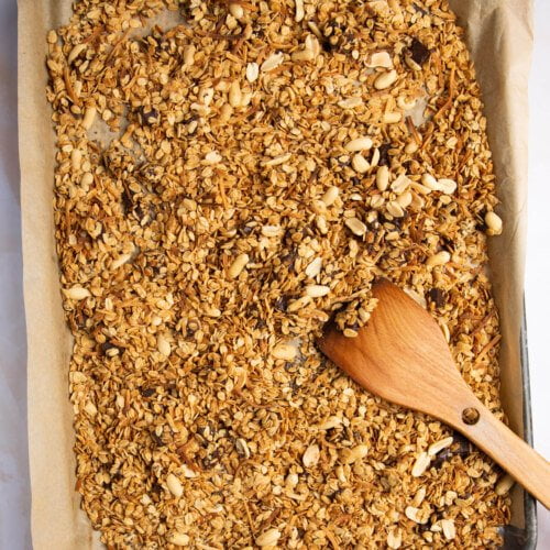 Granola on a baking sheet with a wooden spoon.