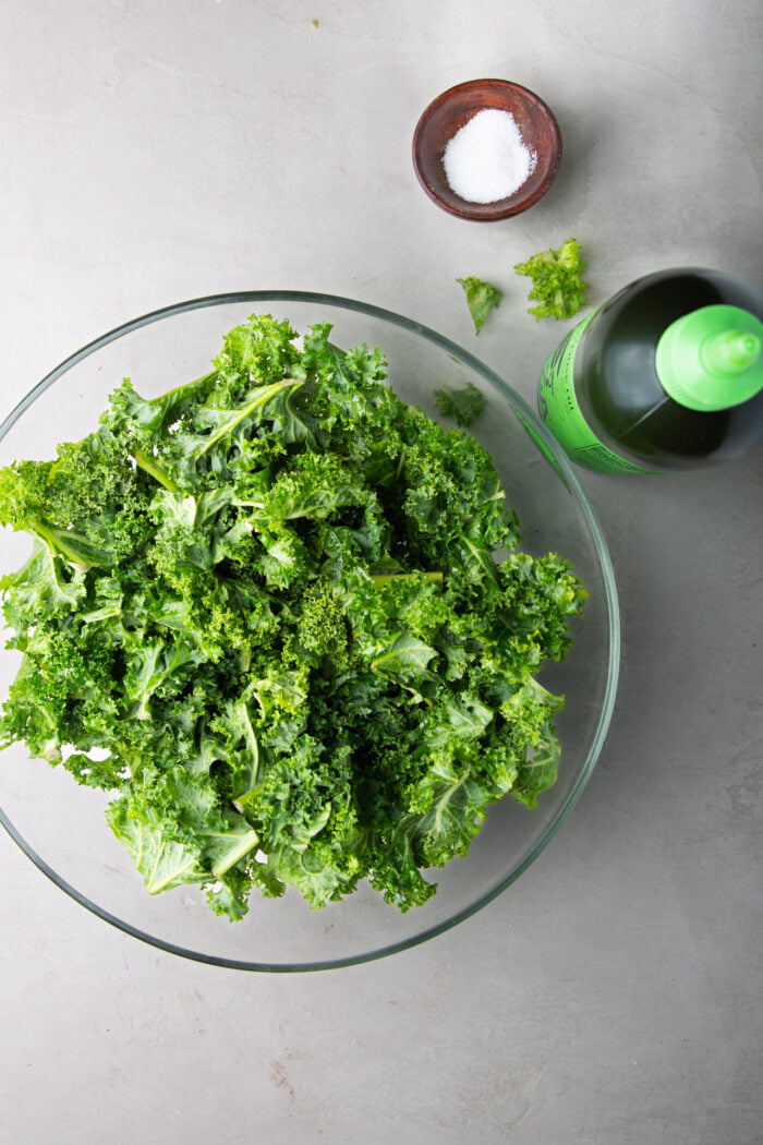 kale in a glass salad bowl, a bottle of olive oil and salt.