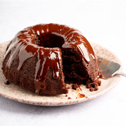 A chocolate bundt cake on a plate with a slice taken out.