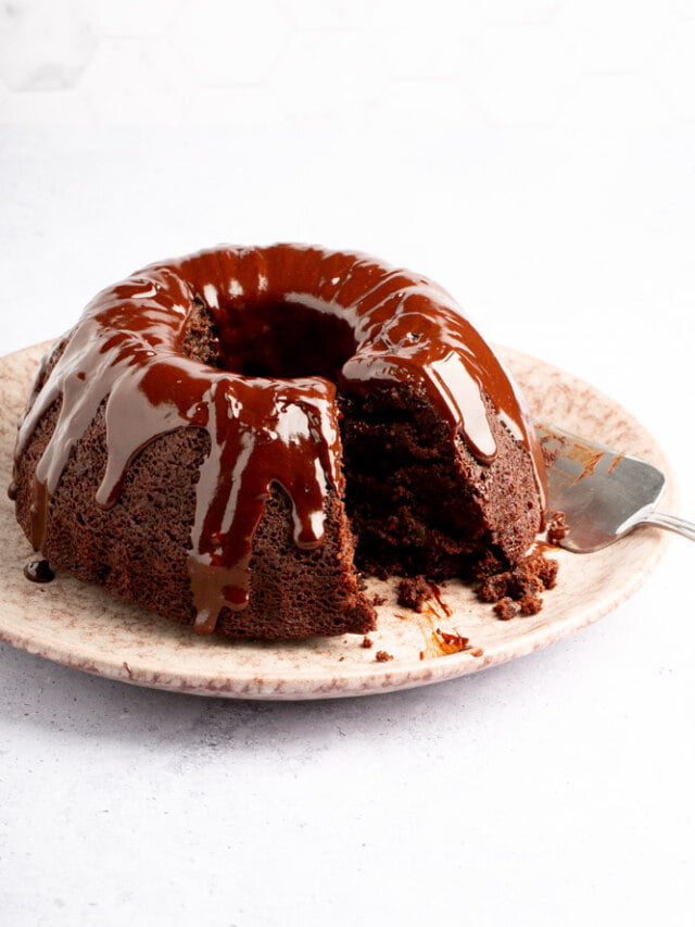 A chocolate bundt cake on a plate with a slice taken out.