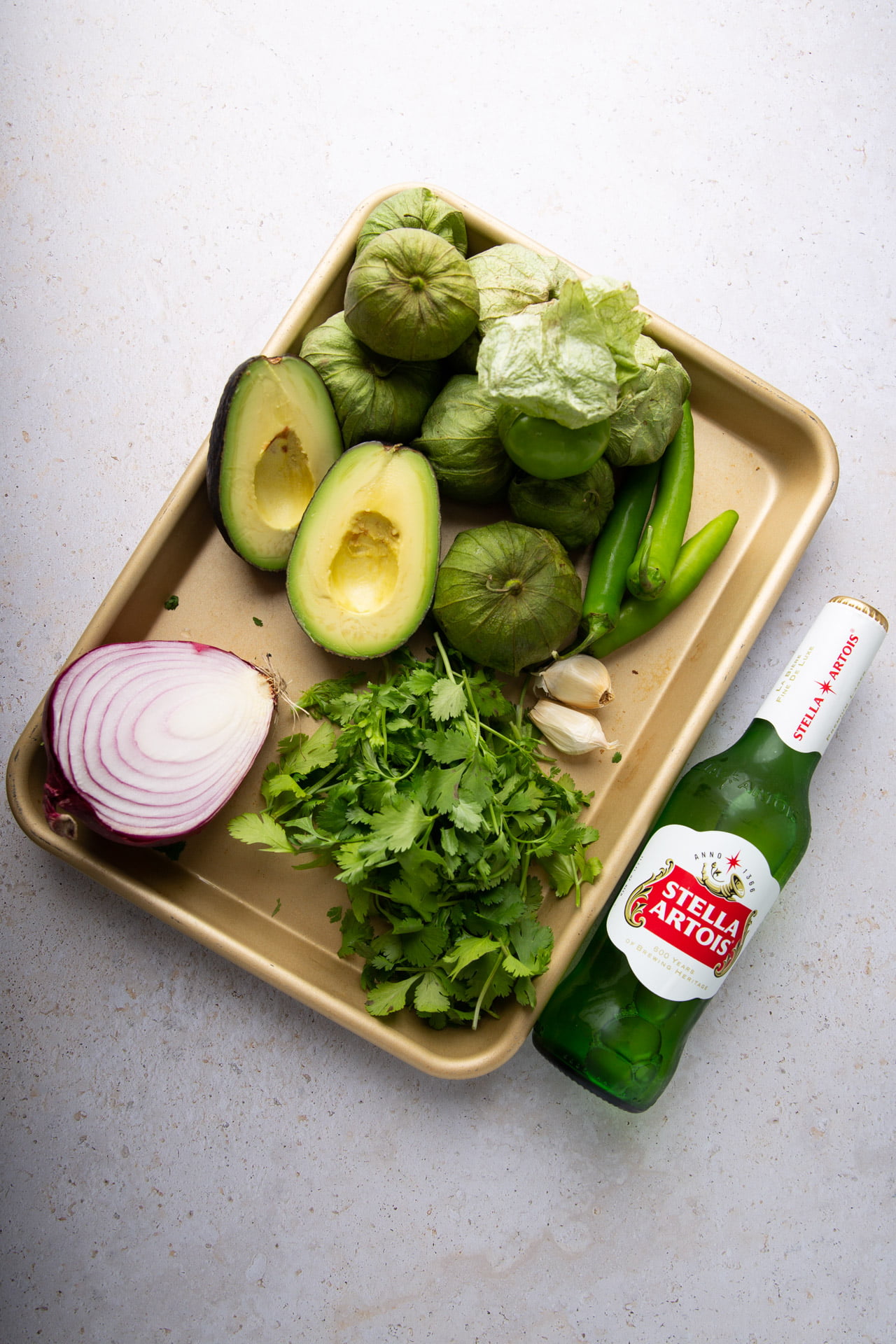 Ingredients for salsa borracha laid out: tomatillos, serrano chiles, cilantro, garlic, beer, avocado, and onion