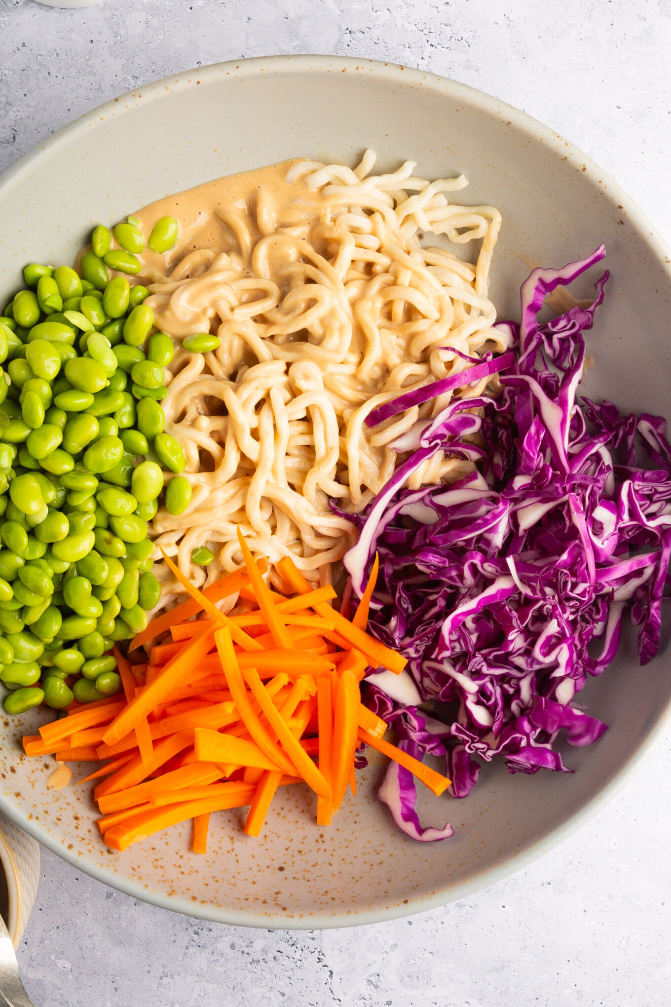 large bowl with noodles, with creamy dressing and red cabagge, Shelled sdamame and juliennned carrots