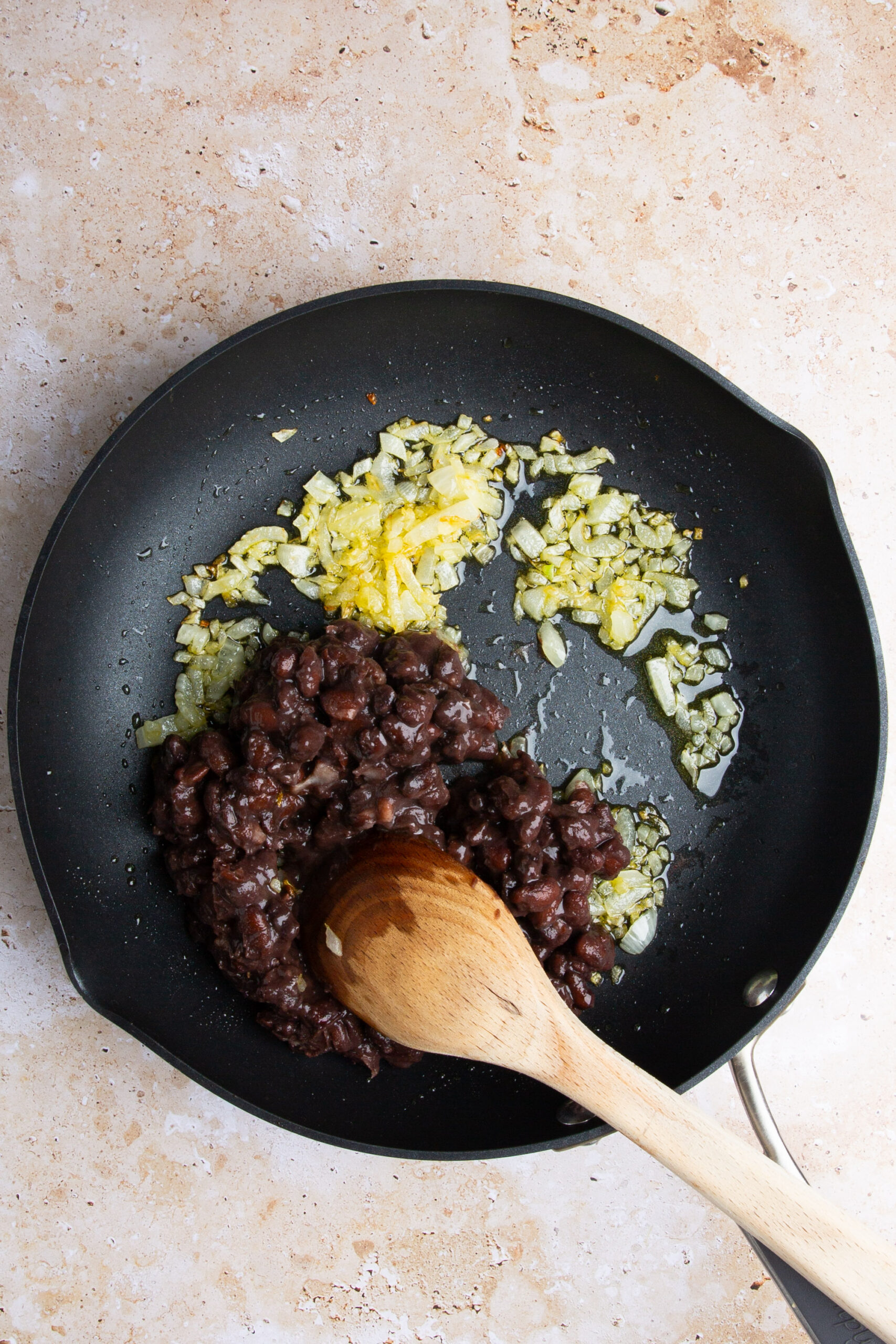 Refried black beans in a skillet with a wooden spoon