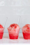 Three cups of watermelon raspado with straws in them.