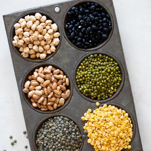 A metal pan filled with 25 essential vegan pantry ingredients including black beans, peas, and lentils.