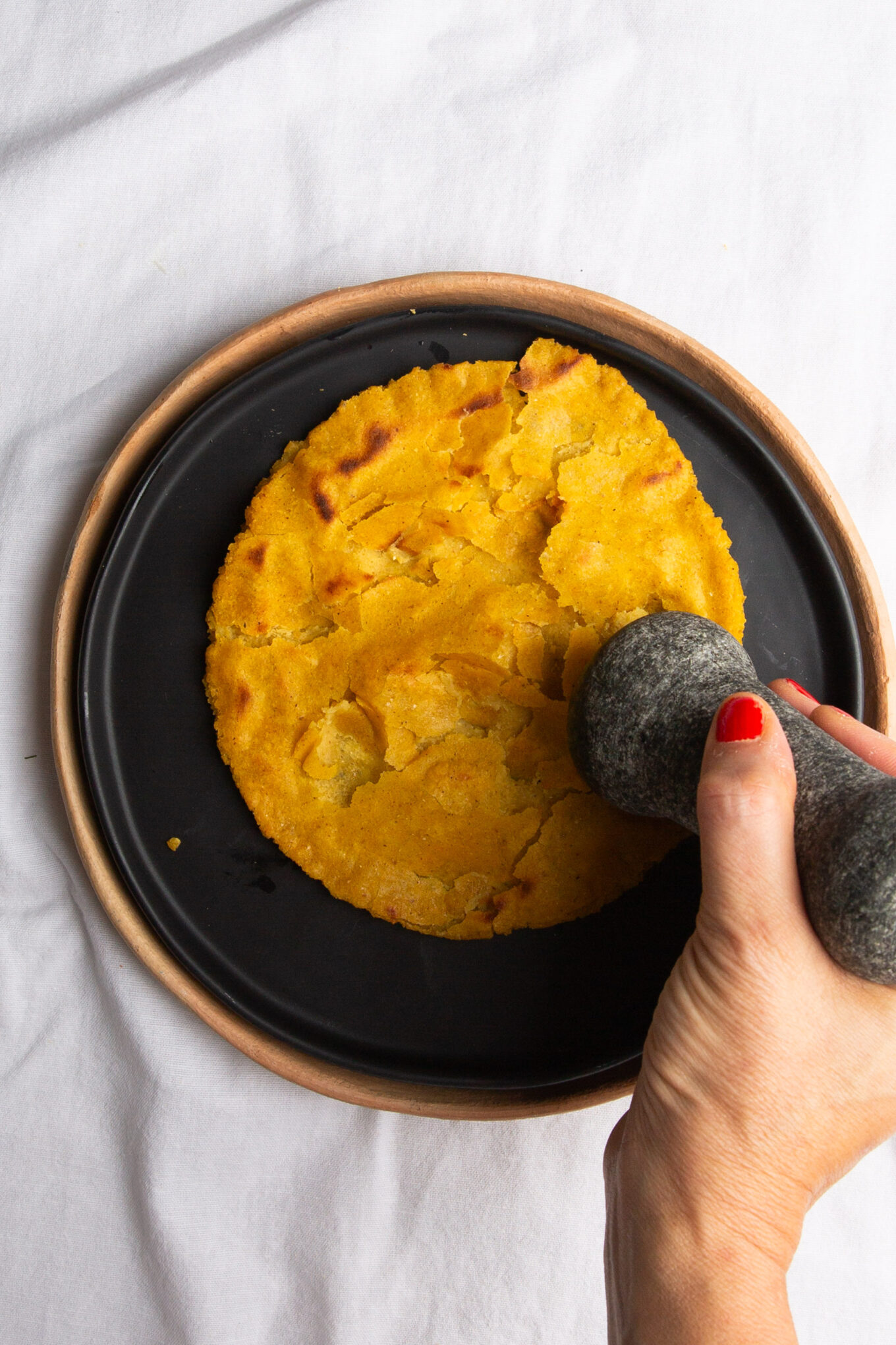 A person using a stone to flatten a tortilla in the traditional Veracruz style.