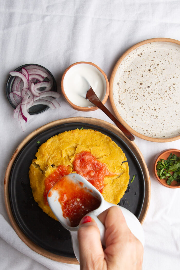 A person is adding Estrujadas Veracruzanas sauce to a plate of food.