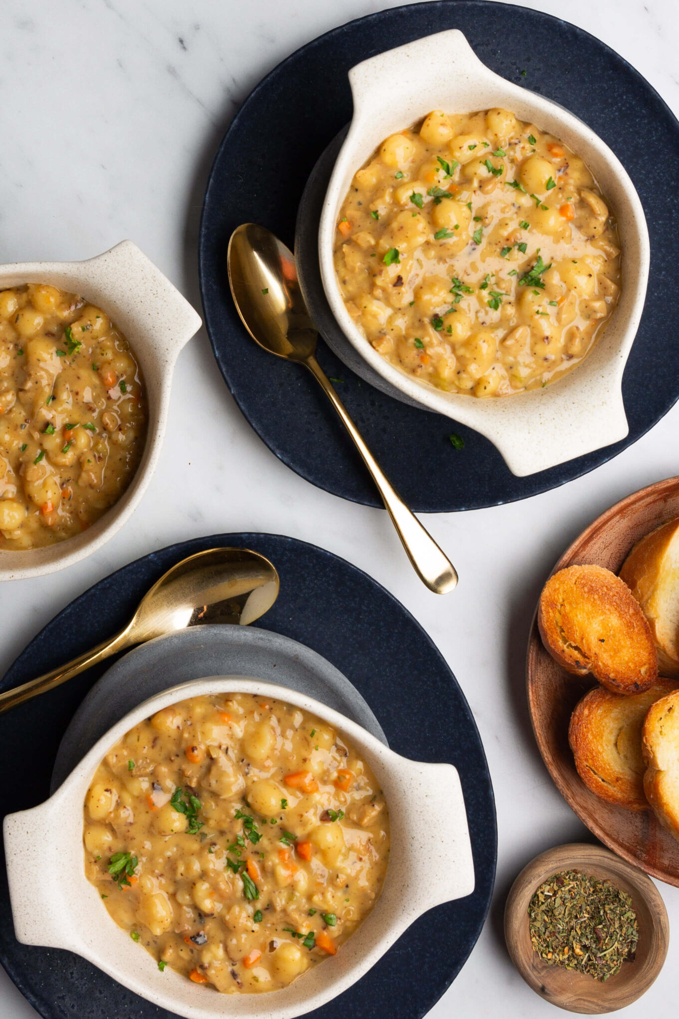 Three bowls of deliciously creamy sausage gnocchi soup and bread on a table.