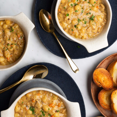 Three bowls of deliciously creamy sausage gnocchi soup and bread on a table.