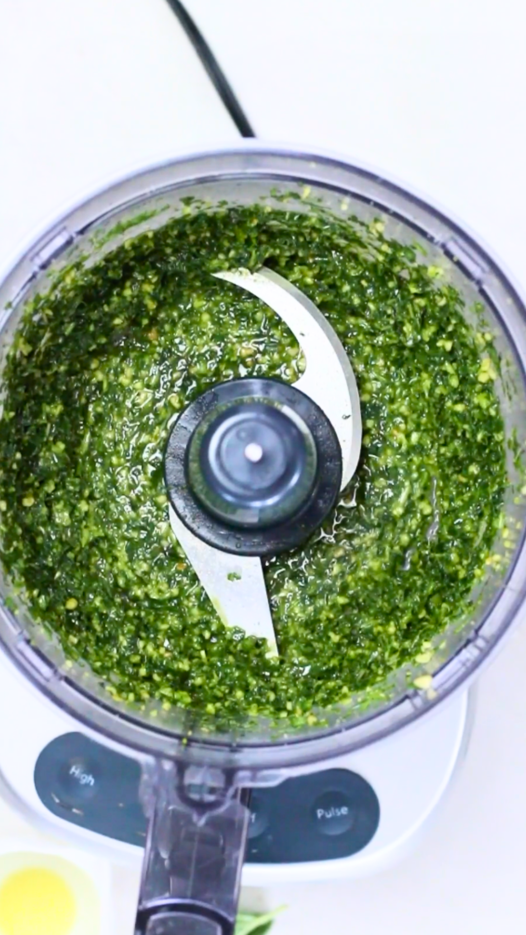 A vegan food processor filled with green pesto.