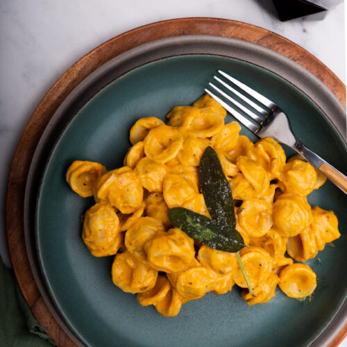 Creamy Vegan Pumpkin Pasta topped with a sprig of sage, served with a fork.