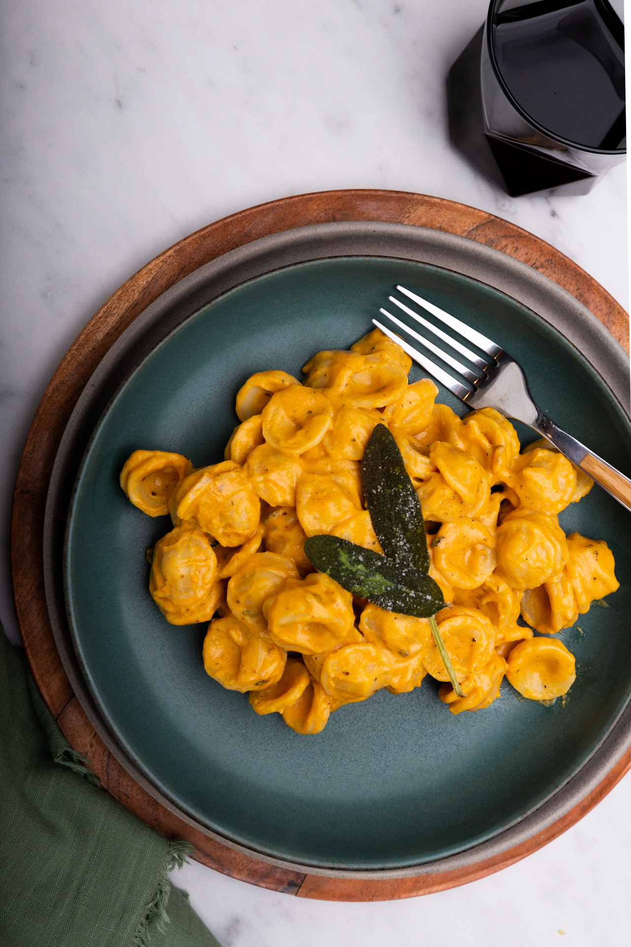 Creamy Vegan Pumpkin Pasta topped with a sprig of sage, served with a fork.