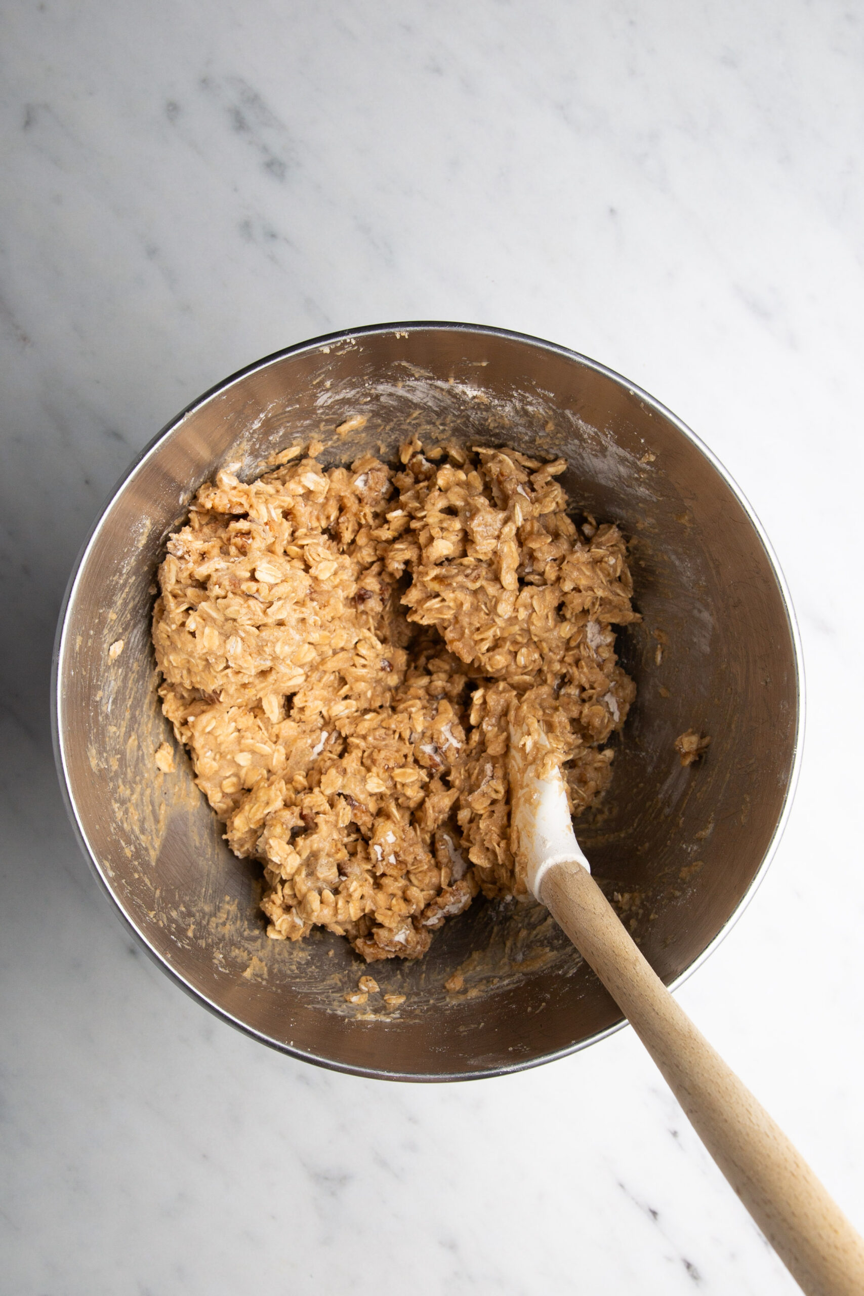 A metal bowl with a wooden spoon filled with delicious oatmeal cookies.