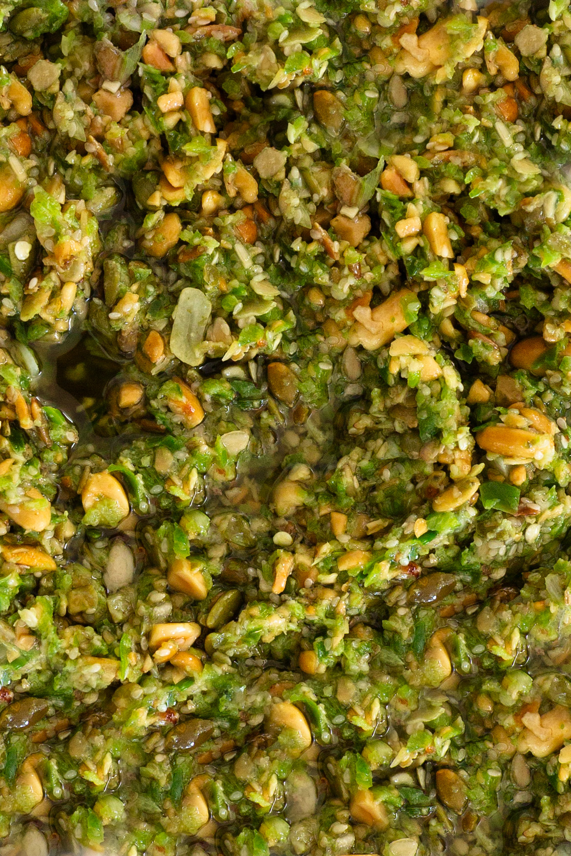 A close up of a bowl of green pesto with pumpkin seeds.