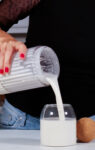 A woman pouring milk into a glass to make the best homemade vegan heavy cream.
