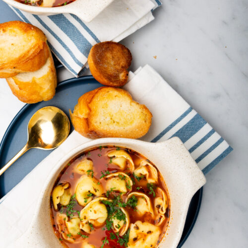 Two bowls of healthy soup with bread on a table.