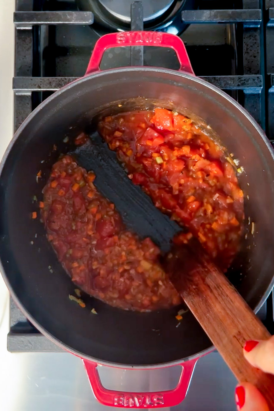 A person stirs a sauce in a pan on the stove.